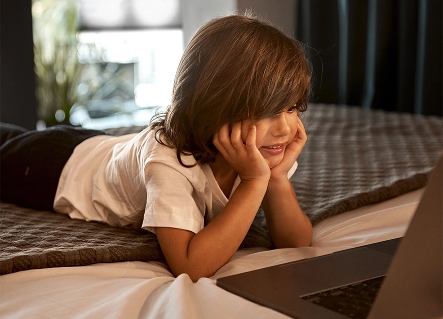 Child laying on the bed playing on a laptop